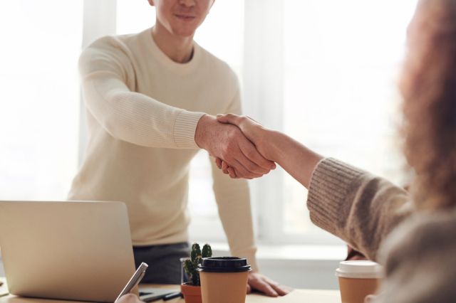 a man standing over a desk shaking hands with a woman sitting opposite him after a successful job interview