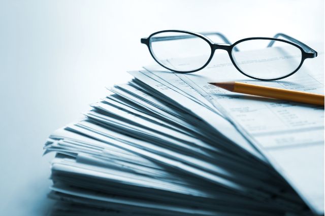 a pair of glasses and a pencil sitting on top of a large pile of paperwork