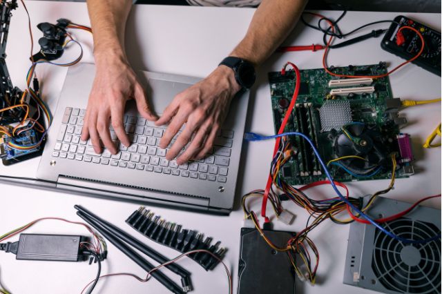 a view from above of a desk full of electronics and paper work with hands working on a laptop