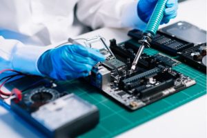 hands wearing blue runner gloves working on an electronics circuit board