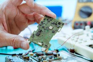 Close up of a hand holding an electronics circuit board thats is being built