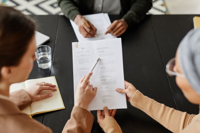 3 people sat around a desk all looking at a CV together