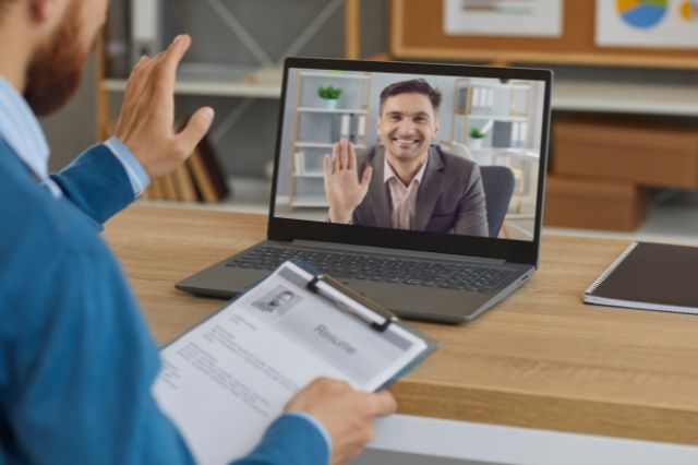 An interviewer waving at an interviewee on a laptop screen during a remote interview