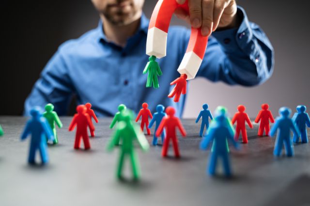 a man holding a large magnet above miniature figurines and attracting some to the magnet