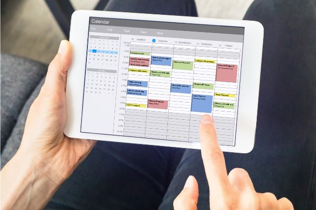 a close up fo hands holding an ipad showing a calendar blocked out into organised time slots