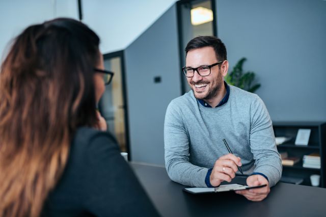 a man sitting at a desk smiling across at the woman interviewing him