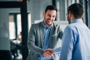 two men in suits shaking hands and smiling at each other