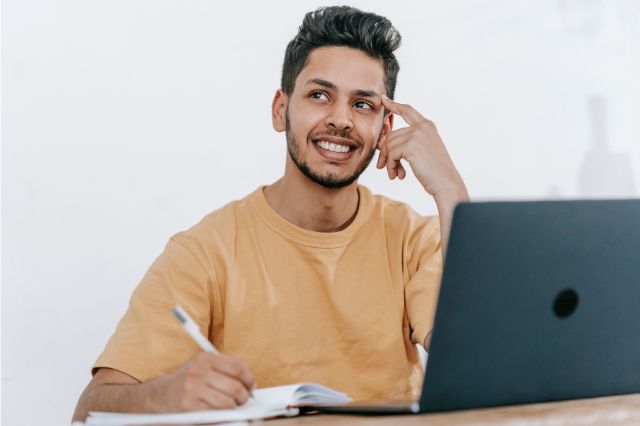 a young man sitting at his laptop thinking about what to write in his LinkedIn personal summary