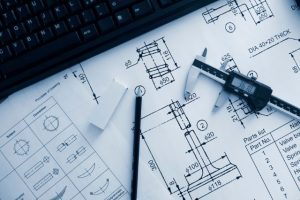 A mechanical design engineers drawings, pencil and tools sitting on an open notebook