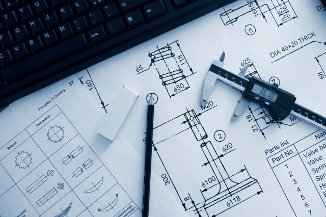 A mechanical design engineers drawings, pencil and tools sitting on an open notebook