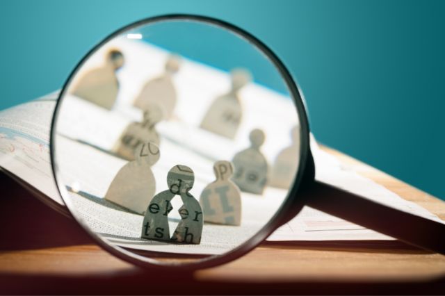a hand held magnifying glass held up to some paper figures to visualise looking for a new recruit