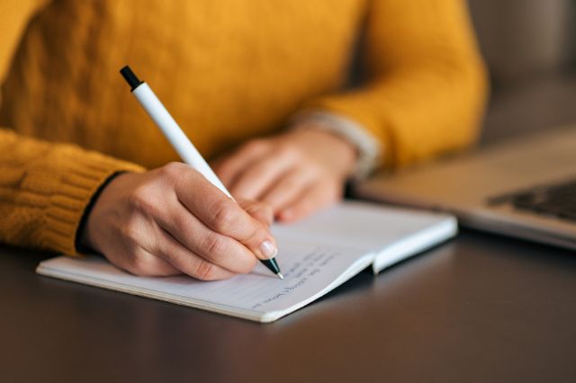 a man sitting at a desk writing a cover letter into a notepad
