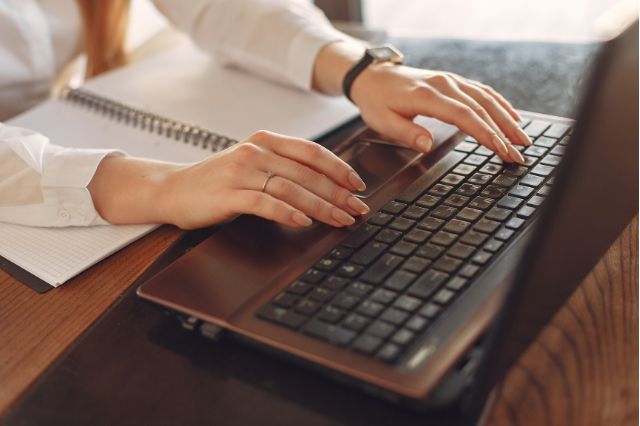a womens hands typing on a alaptop at her desk as she writes out her cover letter