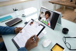 an interviewer holding a CV and looking at a screen with a candidate on the other side